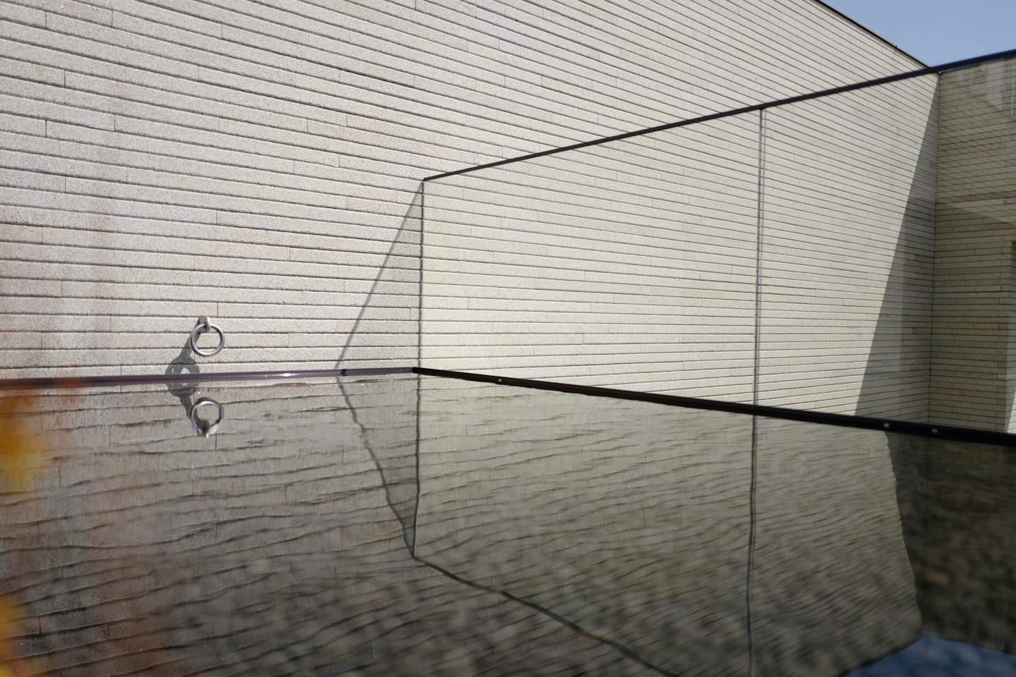 Geometric shadows from a glass railing fall across a textured wall.
