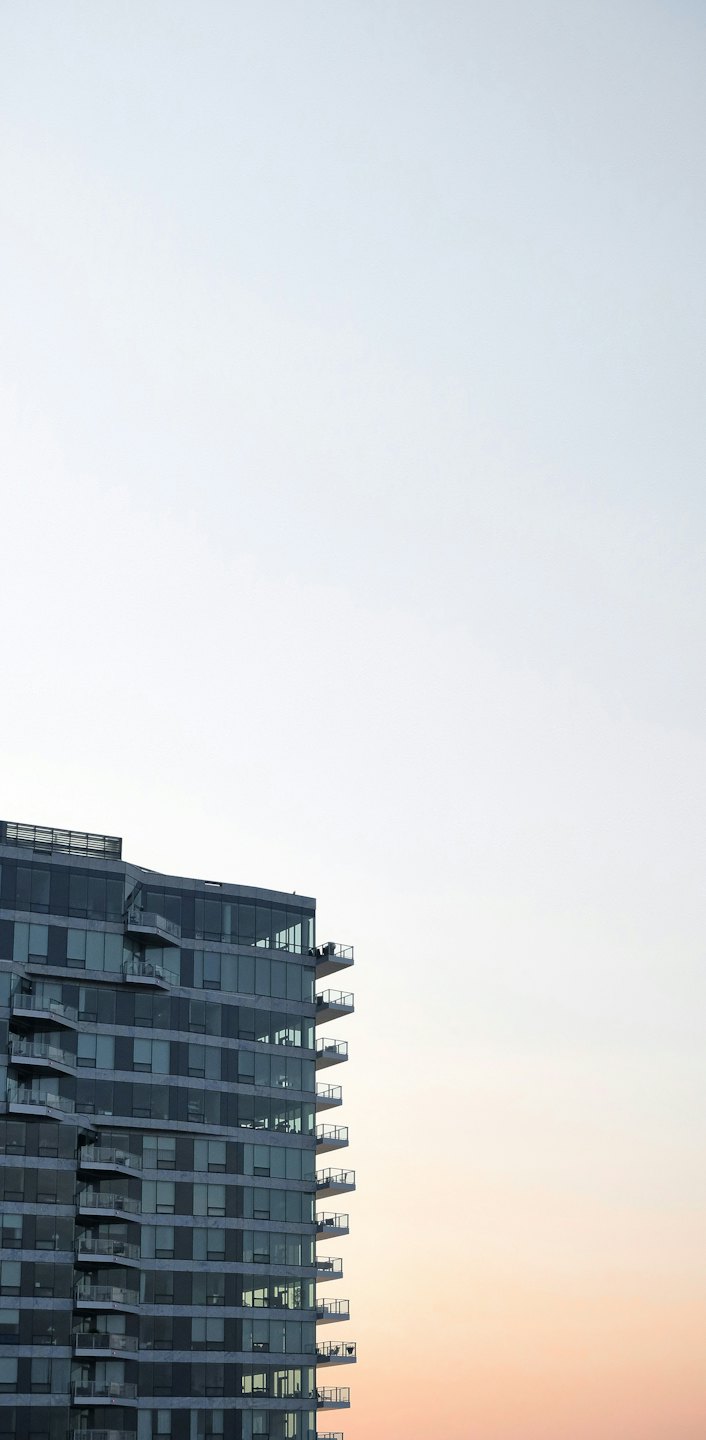 Modern glass apartment building with balconies against a twilight sky.