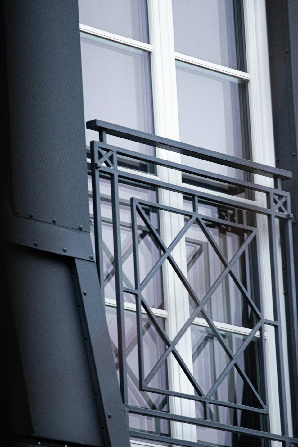 Ornate grey metal railing with diamond patterns in front of window.