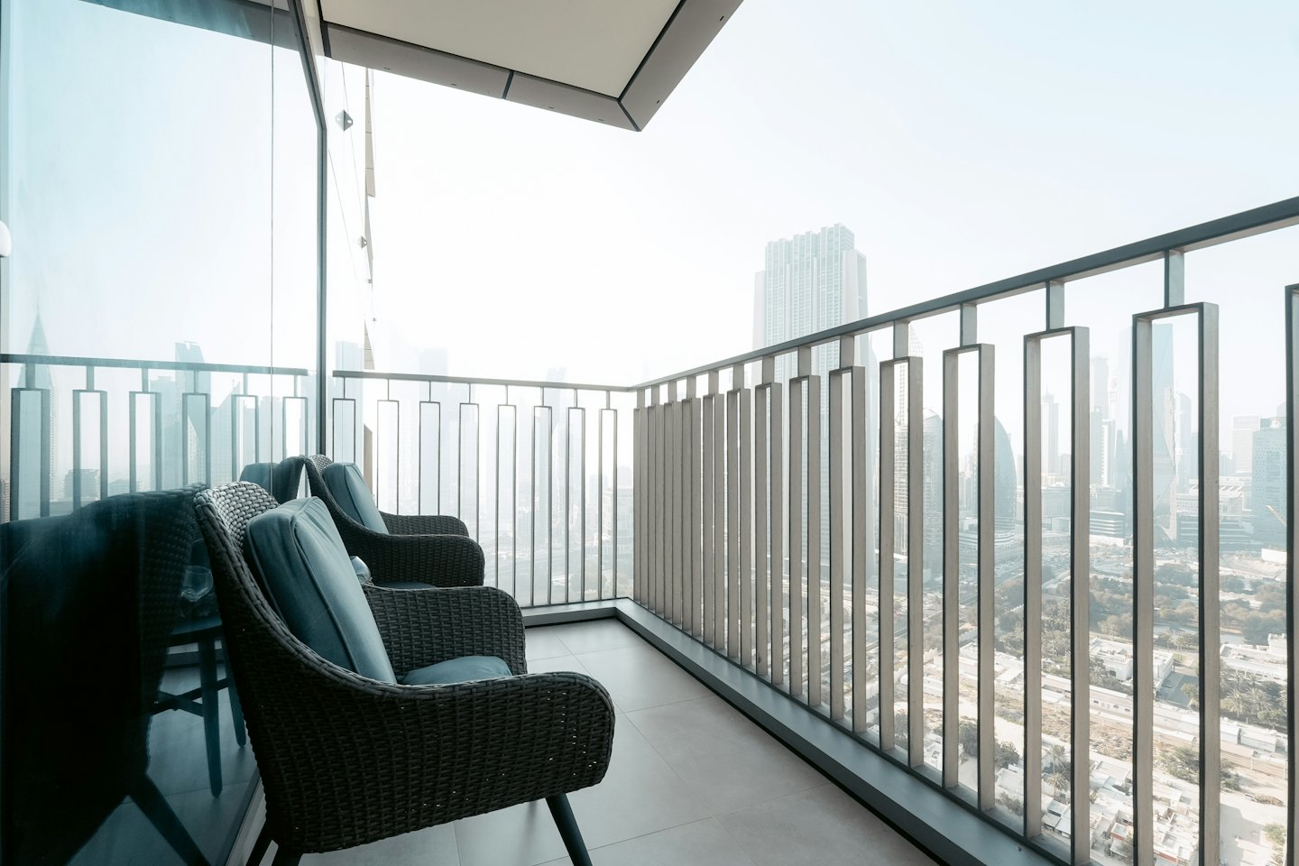 Two wicker chairs on a balcony overlooking the city skyline.
